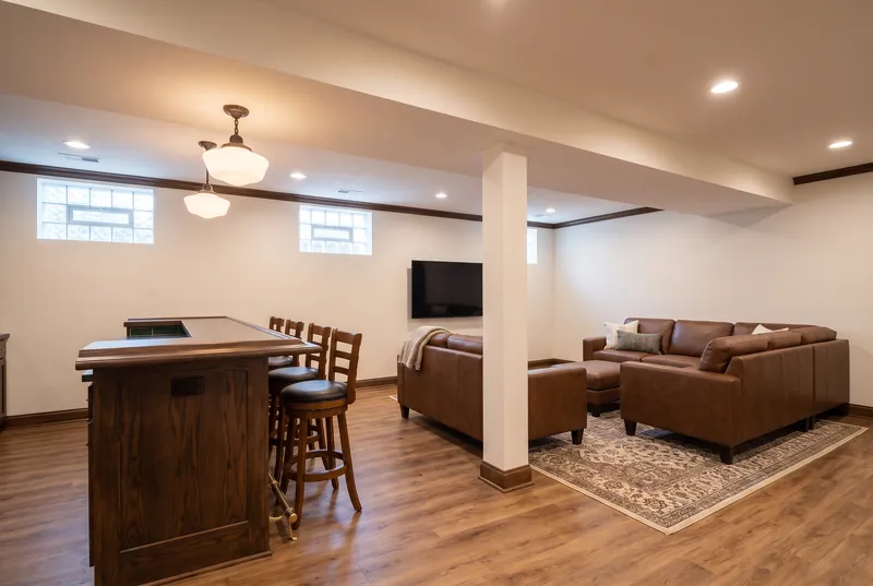 Basement family room with a brown leather sectional, patterned rug and glass block windows