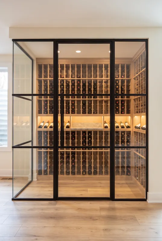Glass enclosed basement wine room with a black steel door and floor to ceiling white oak wine racks