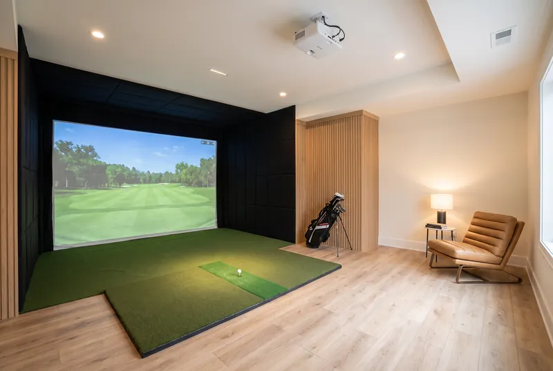Basement golf simulator room with an impact screen, hitting mat and a leather lounge chair