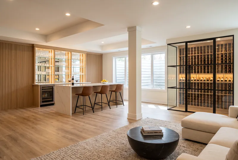 After: Finished lower level with a long white oak bar, waterfall quartz counter, glass wine room and a cream sectional