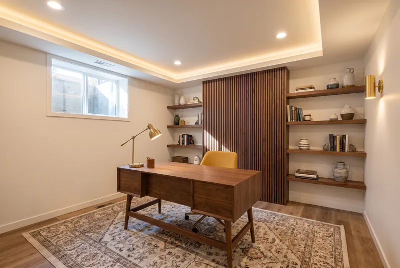 Basement home office with a walnut desk, a mustard chair, a slatted walnut wall and floating shelves