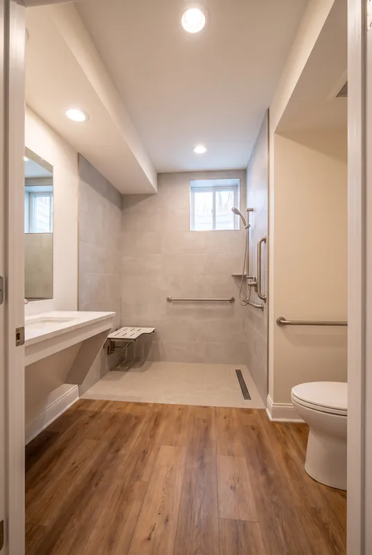 Accessible basement bathroom with a curbless shower, fold down seat, grab bars and a wall hung vanity