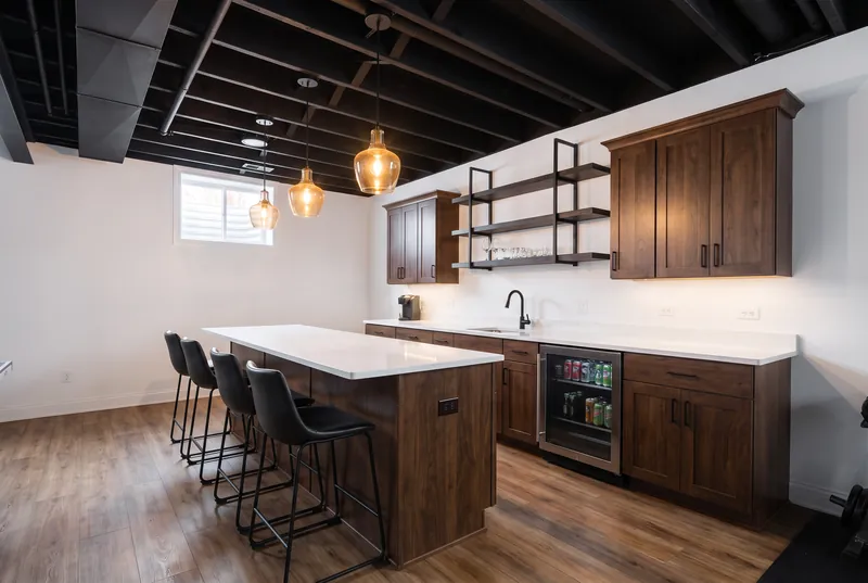 Basement wet bar with dark walnut cabinets, a white quartz counter, black metal shelving and pendants under a black open ceiling