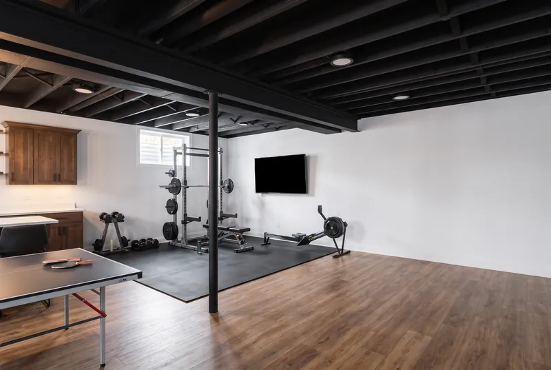 Basement gym with a rubber floor, squat rack and dumbbells beside a ping pong table