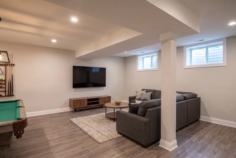 Basement TV area with a charcoal sofa, walnut console and the corner of a pool table