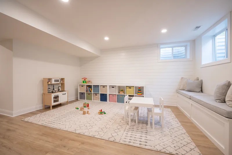 Basement kids' play area with built in cubbies, a window seat, play kitchen and a small table