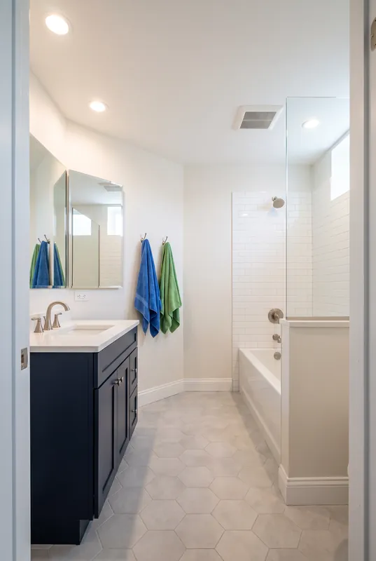 Basement bathroom with a tub and shower, white subway tile, navy vanity and hexagon floor tile